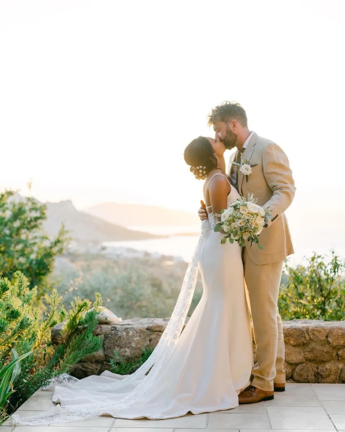 Bride and groom on the stone wall above the Saronic at sunset