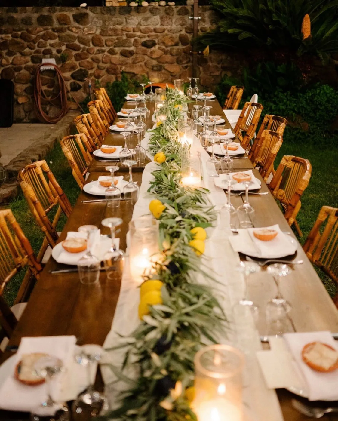 A long banquet table set with candles along the stone wall